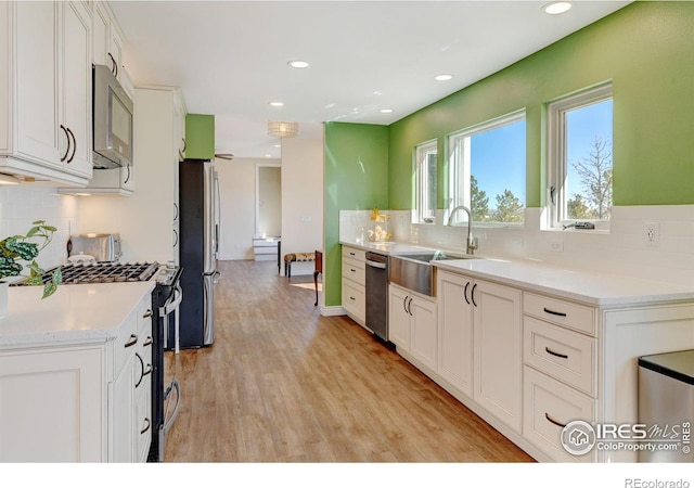 kitchen with white cabinets, appliances with stainless steel finishes, light countertops, light wood-style floors, and a sink