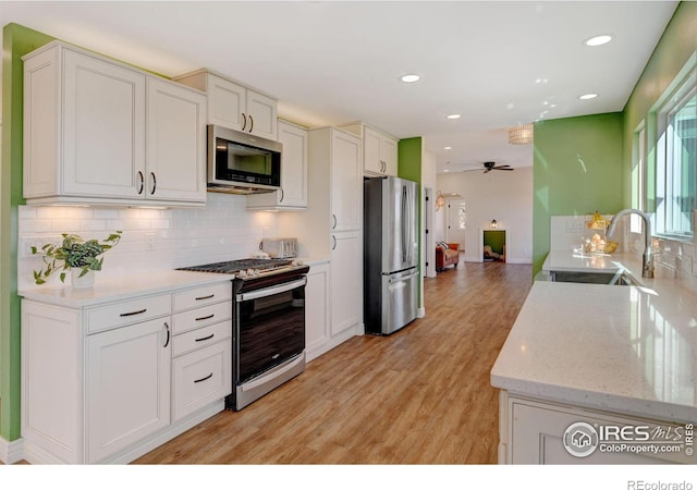 kitchen featuring light wood-style flooring, a sink, white cabinets, appliances with stainless steel finishes, and backsplash