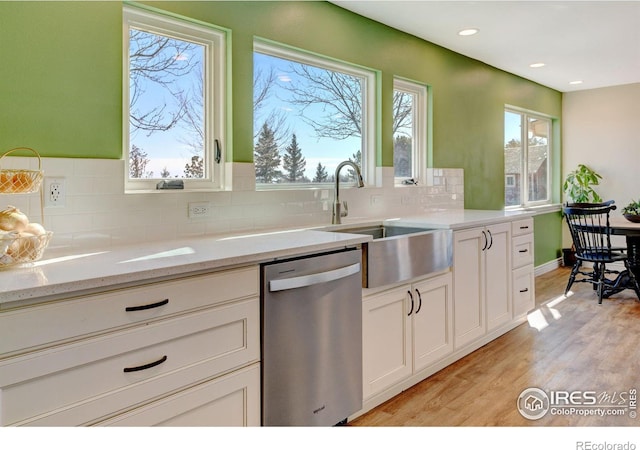 kitchen featuring light stone counters, a sink, light wood-style floors, dishwasher, and tasteful backsplash