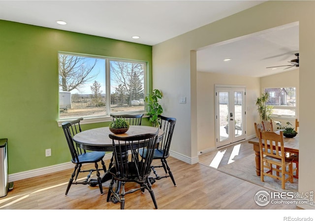 dining space with a healthy amount of sunlight, light wood-style flooring, baseboards, and french doors