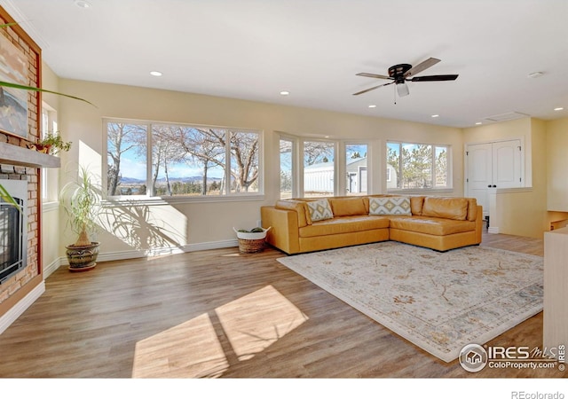 living room with recessed lighting, a ceiling fan, baseboards, light wood-style floors, and a brick fireplace