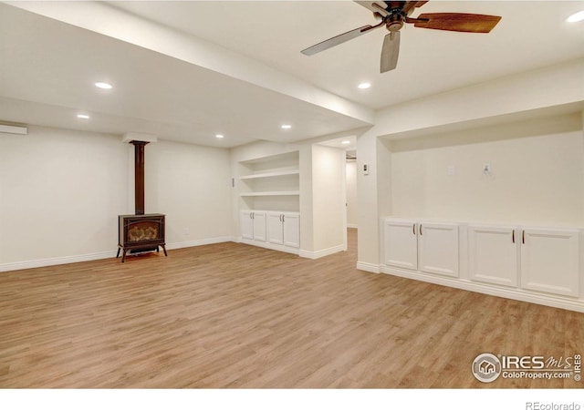 interior space featuring light wood-style floors, recessed lighting, a wood stove, and built in shelves