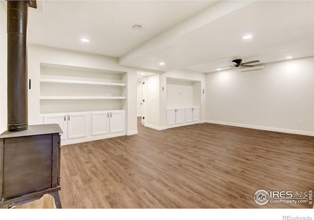 unfurnished living room with a ceiling fan, a wood stove, baseboards, and light wood finished floors