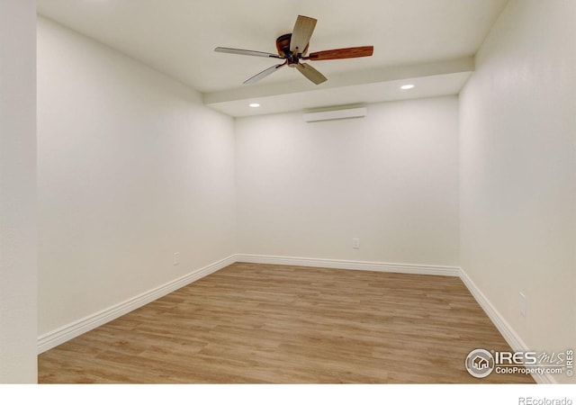 empty room featuring baseboards, ceiling fan, light wood-type flooring, and a wall mounted air conditioner