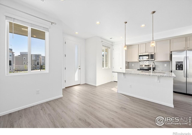 kitchen with stainless steel appliances, a sink, light wood finished floors, and tasteful backsplash