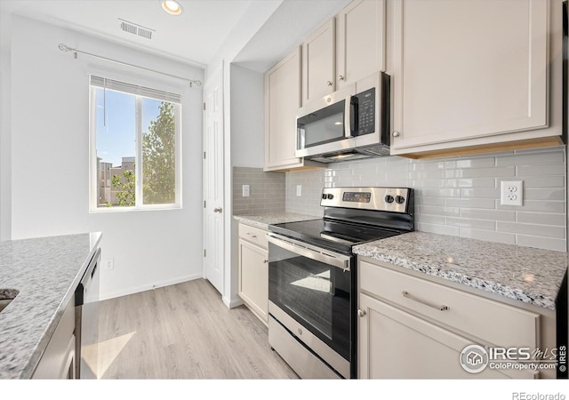 kitchen featuring visible vents, light wood-style flooring, backsplash, appliances with stainless steel finishes, and light stone countertops