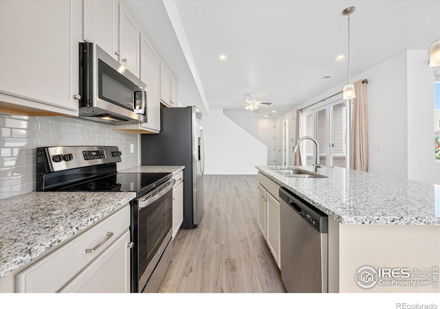 kitchen featuring a center island with sink, ceiling fan, appliances with stainless steel finishes, a sink, and backsplash