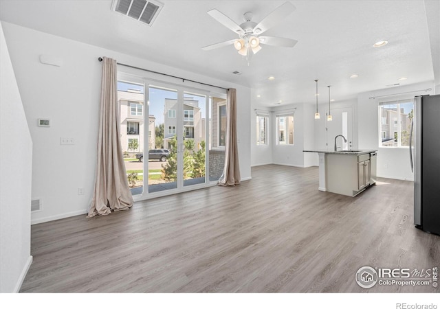 unfurnished living room with baseboards, light wood-style flooring, visible vents, and a sink