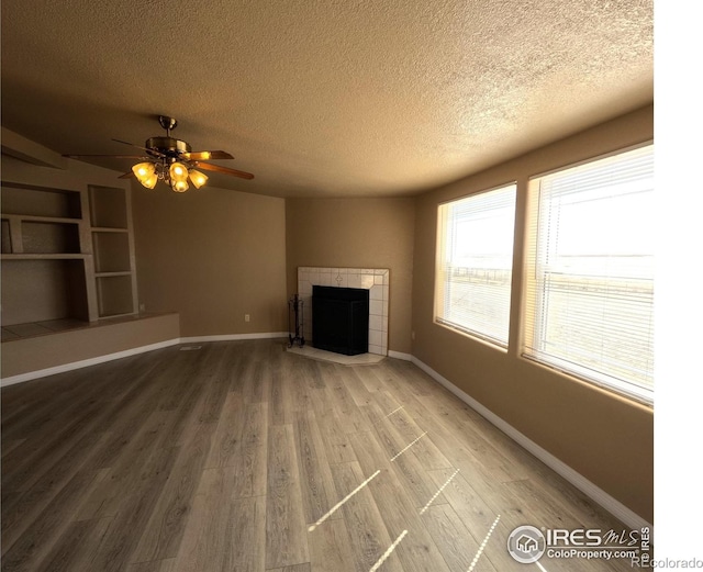 unfurnished living room with a textured ceiling, a fireplace, wood finished floors, and baseboards