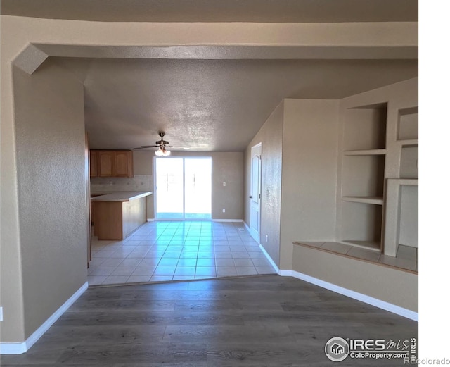 interior space with built in features, light wood-style floors, ceiling fan, a textured ceiling, and baseboards