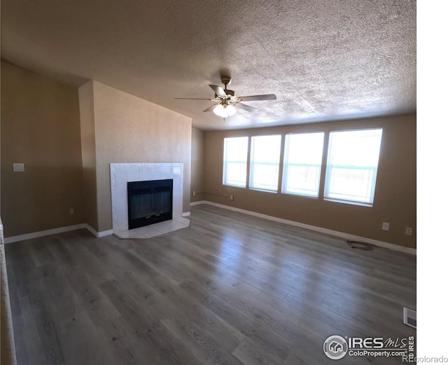 unfurnished living room with a fireplace, a ceiling fan, a textured ceiling, wood finished floors, and baseboards