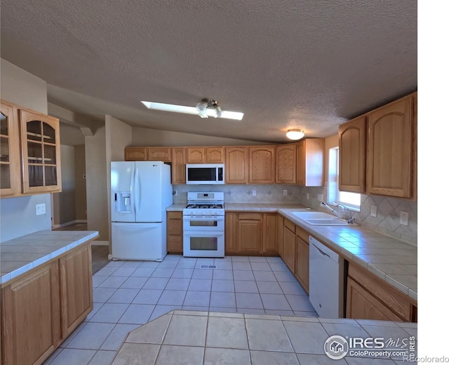 kitchen featuring white appliances, light tile patterned flooring, a sink, and tile countertops