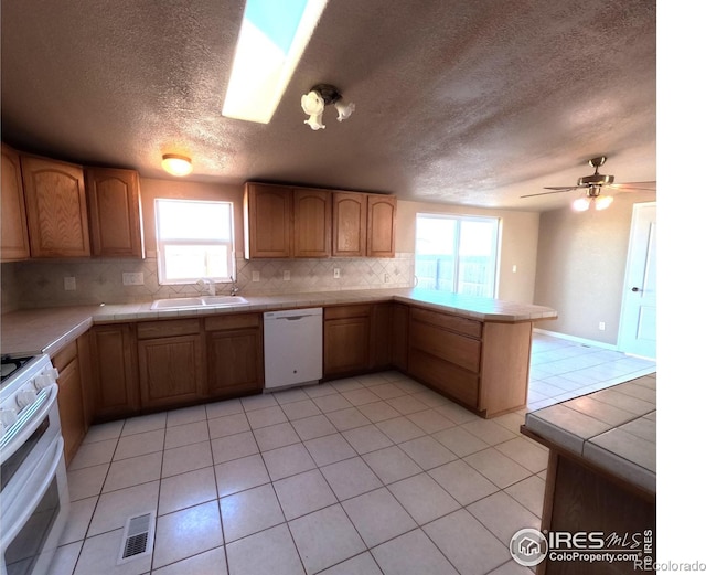 kitchen featuring white appliances, tasteful backsplash, visible vents, a peninsula, and a sink