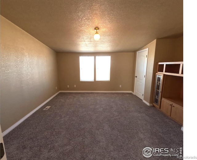 spare room with a textured ceiling, carpet flooring, visible vents, and baseboards