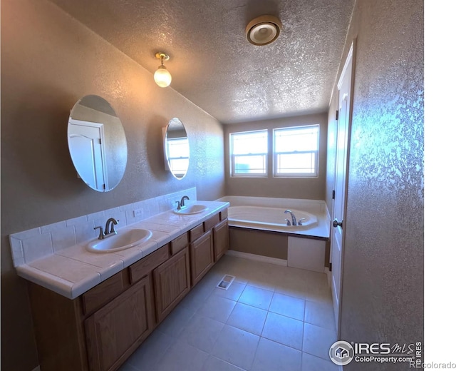 bathroom with a textured wall, tile patterned floors, a garden tub, a textured ceiling, and a sink