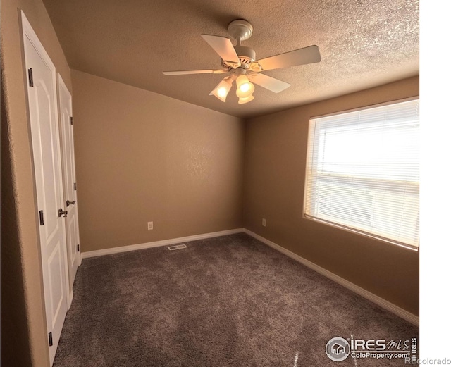 unfurnished bedroom with visible vents, baseboards, ceiling fan, dark colored carpet, and a textured ceiling