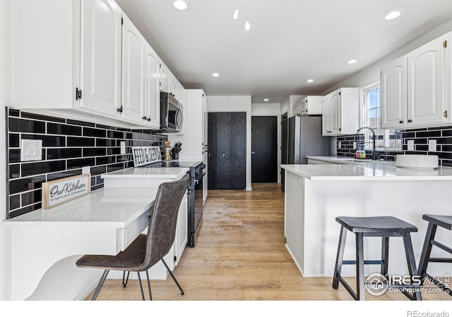 kitchen featuring a breakfast bar area, stainless steel appliances, white cabinets, a sink, and a peninsula