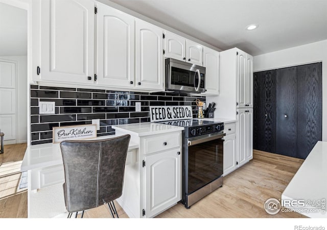 kitchen with tasteful backsplash, electric stove, stainless steel microwave, light wood-style floors, and white cabinetry