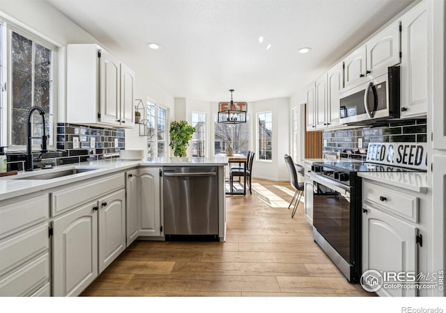 kitchen featuring light wood-style flooring, a peninsula, stainless steel appliances, white cabinetry, and a sink