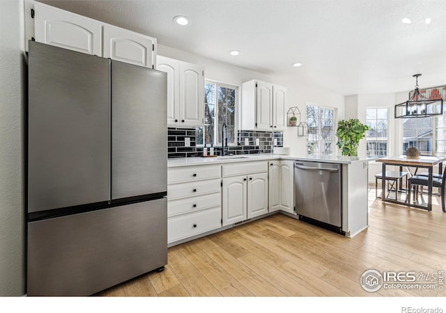 kitchen featuring light wood finished floors, stainless steel appliances, white cabinetry, a sink, and a peninsula