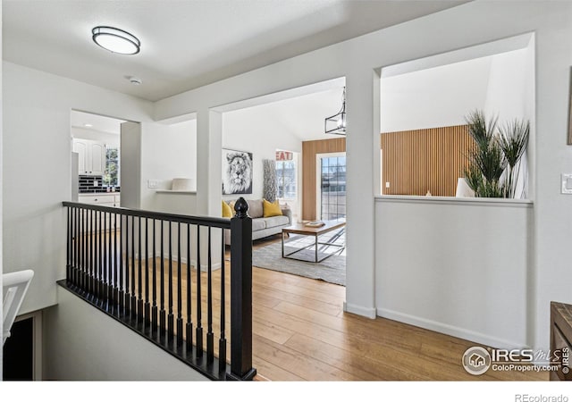 hallway with a chandelier, baseboards, hardwood / wood-style floors, and an upstairs landing