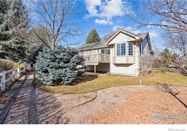 view of side of property featuring fence, a lawn, and a wooden deck