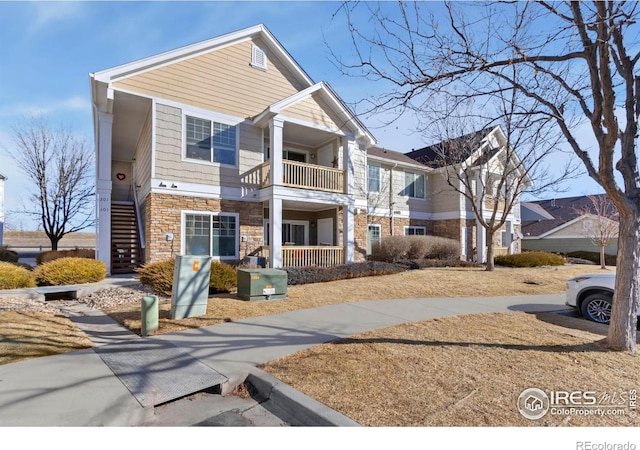 view of front of home featuring stairs, stone siding, and a balcony