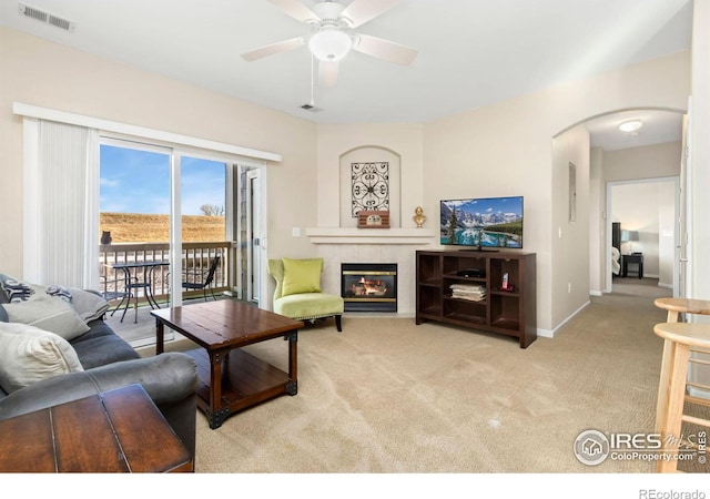 living area featuring arched walkways, carpet, visible vents, a tile fireplace, and baseboards