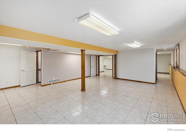 finished basement with visible vents, a textured ceiling, baseboards, and light tile patterned floors