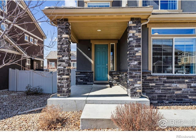 doorway to property with stone siding and fence