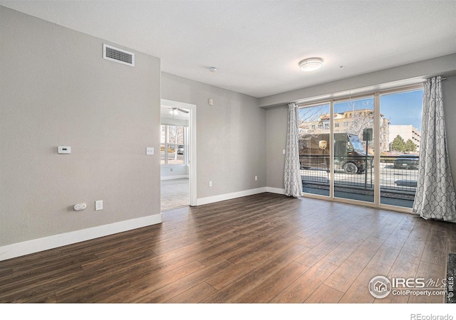 unfurnished room with visible vents, dark wood finished floors, and baseboards