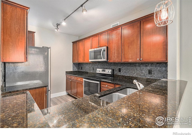 kitchen featuring stainless steel appliances, a sink, light wood-type flooring, decorative backsplash, and dark stone counters