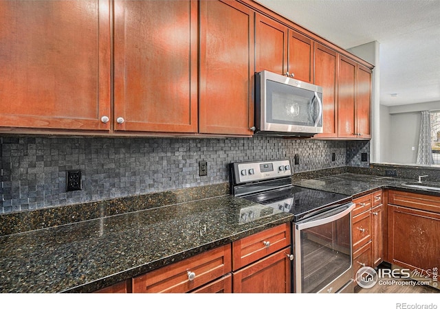 kitchen with tasteful backsplash, brown cabinetry, dark stone counters, appliances with stainless steel finishes, and a sink