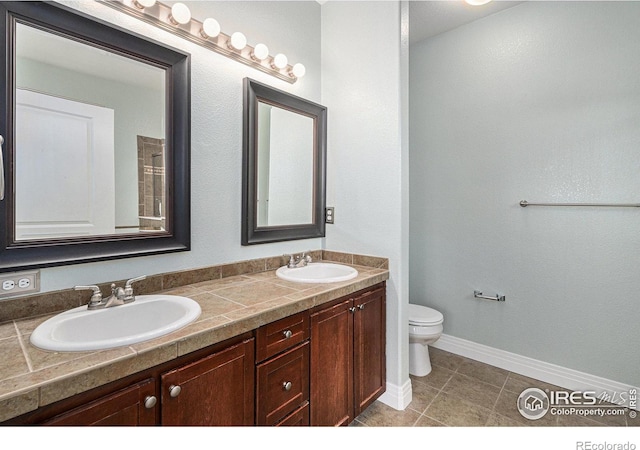 bathroom featuring double vanity, baseboards, toilet, and a sink