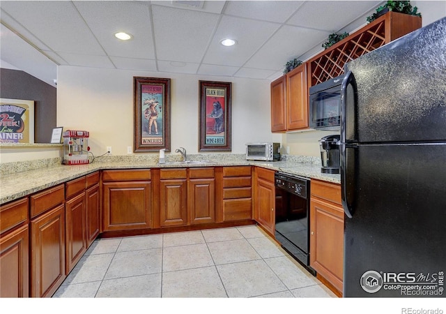 kitchen with light tile patterned floors, light stone counters, brown cabinets, black appliances, and a sink