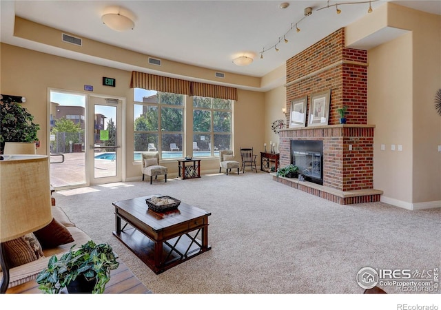 carpeted living area with rail lighting, a brick fireplace, visible vents, and baseboards