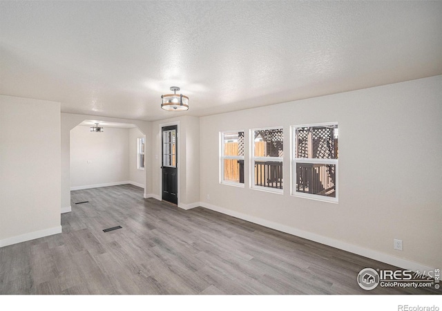 unfurnished room with a notable chandelier, a textured ceiling, baseboards, and wood finished floors