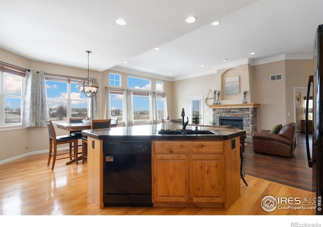 kitchen with black dishwasher, dark countertops, visible vents, a sink, and an island with sink