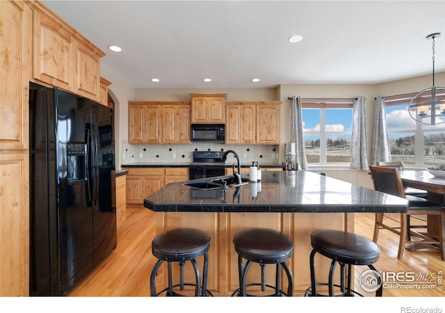 kitchen with a breakfast bar area, a sink, light brown cabinetry, black appliances, and tasteful backsplash