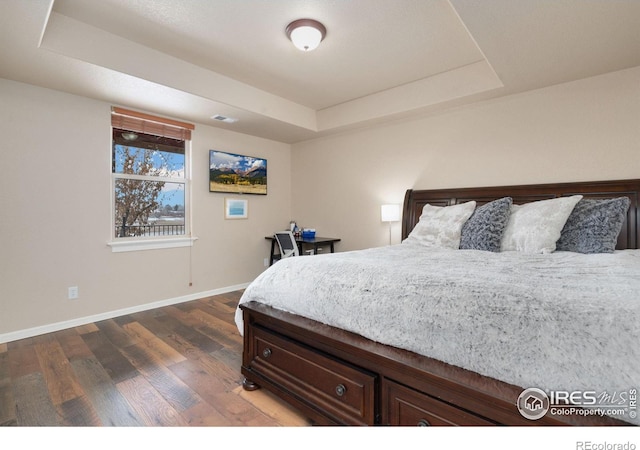 bedroom with dark wood-style floors, a tray ceiling, visible vents, and baseboards