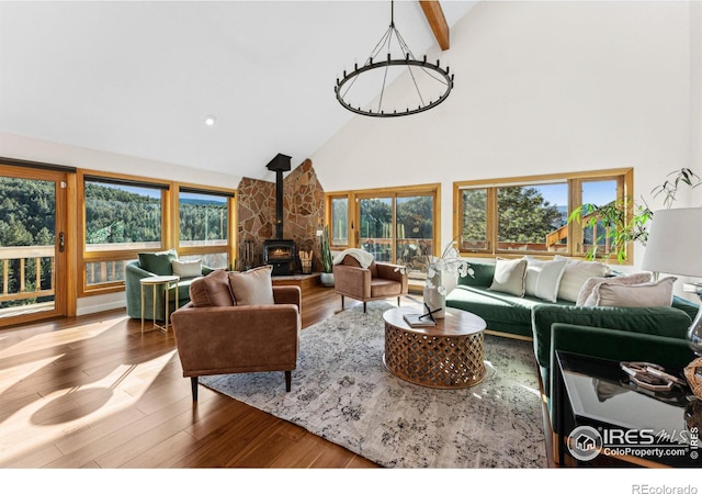 living room with beamed ceiling, a notable chandelier, high vaulted ceiling, wood finished floors, and a wood stove