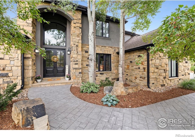 entrance to property with french doors, stone siding, and stucco siding