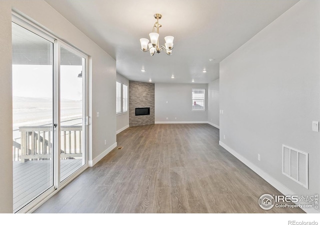 unfurnished living room featuring a chandelier, a large fireplace, wood finished floors, visible vents, and baseboards