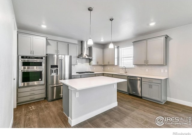 kitchen featuring gray cabinetry, stainless steel appliances, a sink, backsplash, and wall chimney exhaust hood