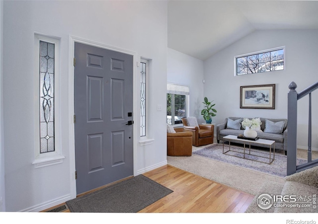 entrance foyer featuring high vaulted ceiling, visible vents, baseboards, and wood finished floors