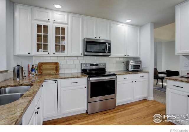 kitchen with white cabinets, appliances with stainless steel finishes, decorative backsplash, light wood finished floors, and glass insert cabinets