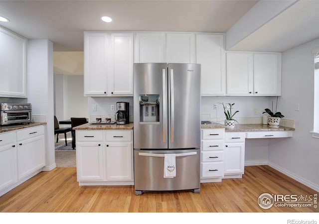 kitchen with a toaster, built in study area, light wood-style flooring, white cabinetry, and stainless steel refrigerator with ice dispenser