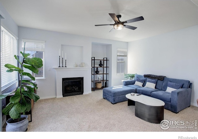 living area featuring ceiling fan, carpet floors, a glass covered fireplace, and baseboards