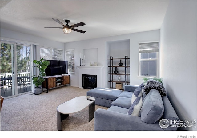 living area featuring ceiling fan, carpet flooring, and a glass covered fireplace