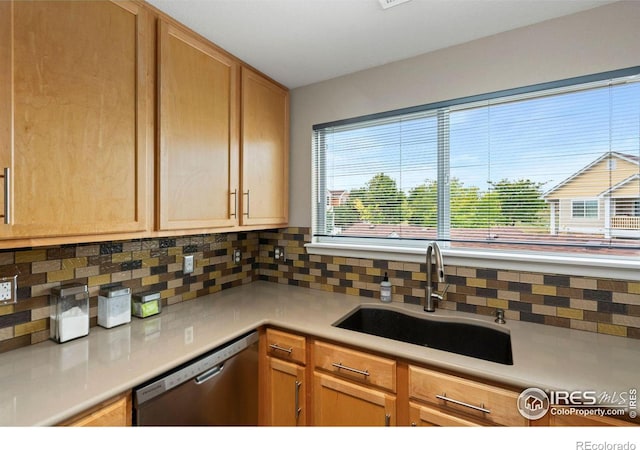 kitchen with stainless steel dishwasher, decorative backsplash, a sink, and light countertops